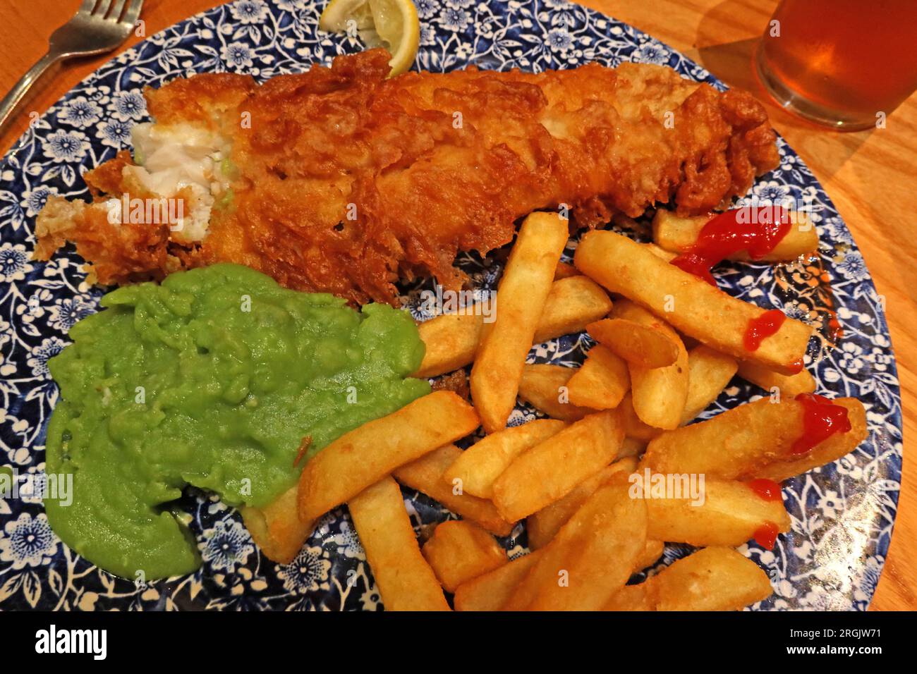 Pesce e patatine fritte tradizionali inglesi, con piselli Mushy. Servita all'interno in un pub con una pinta di amaro Foto Stock