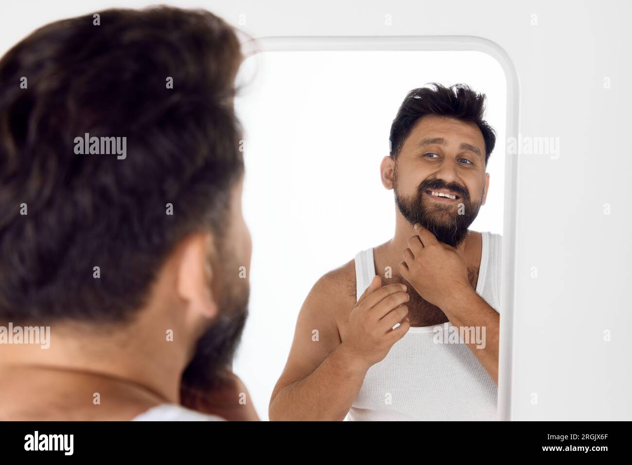 Bello, attraente uomo barbuto in singolare che guarda allo specchio e  sorride, che si prende cura dopo il viso dopo la doccia. Routine mattutina  Foto stock - Alamy