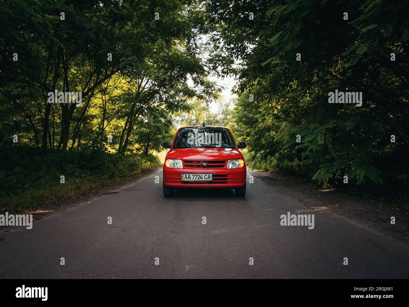 kei car Daihatsu mira L700 su una strada nella foresta decidua. Vista frontale di una piccola auto rossa che attraversa il bosco. Foto Stock