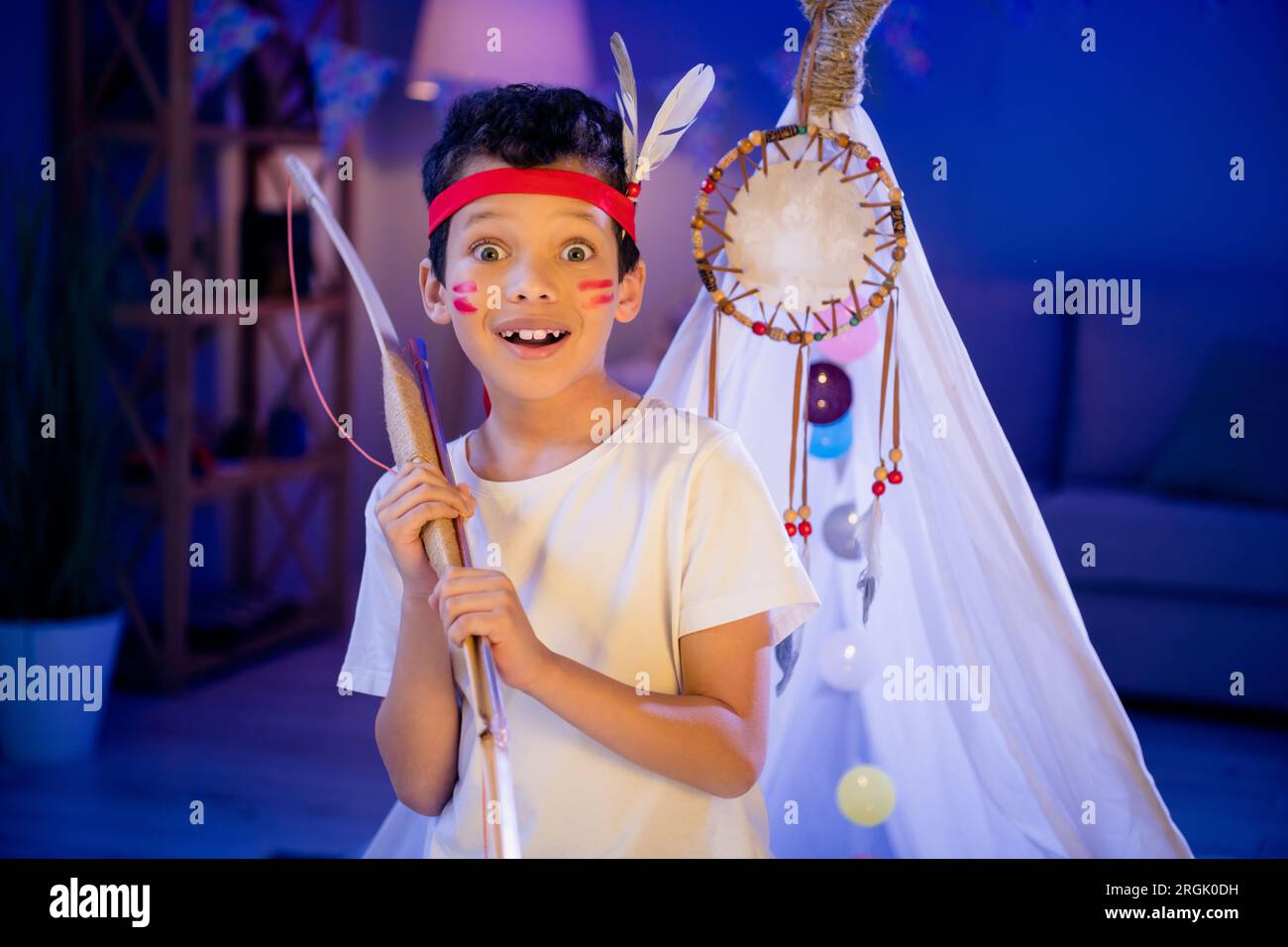 Foto di un ragazzo sorpreso felice in costume tradizionale che interpreta il personaggio preferito dei nativi americani nella sala giochi per le feste di sonno Foto Stock