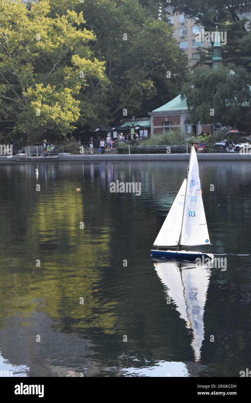 Una barca giocattolo che naviga su Conservatory Water, lo stagno delle barche a Central Park, New York, con la Boathouse sullo sfondo. Foto Stock