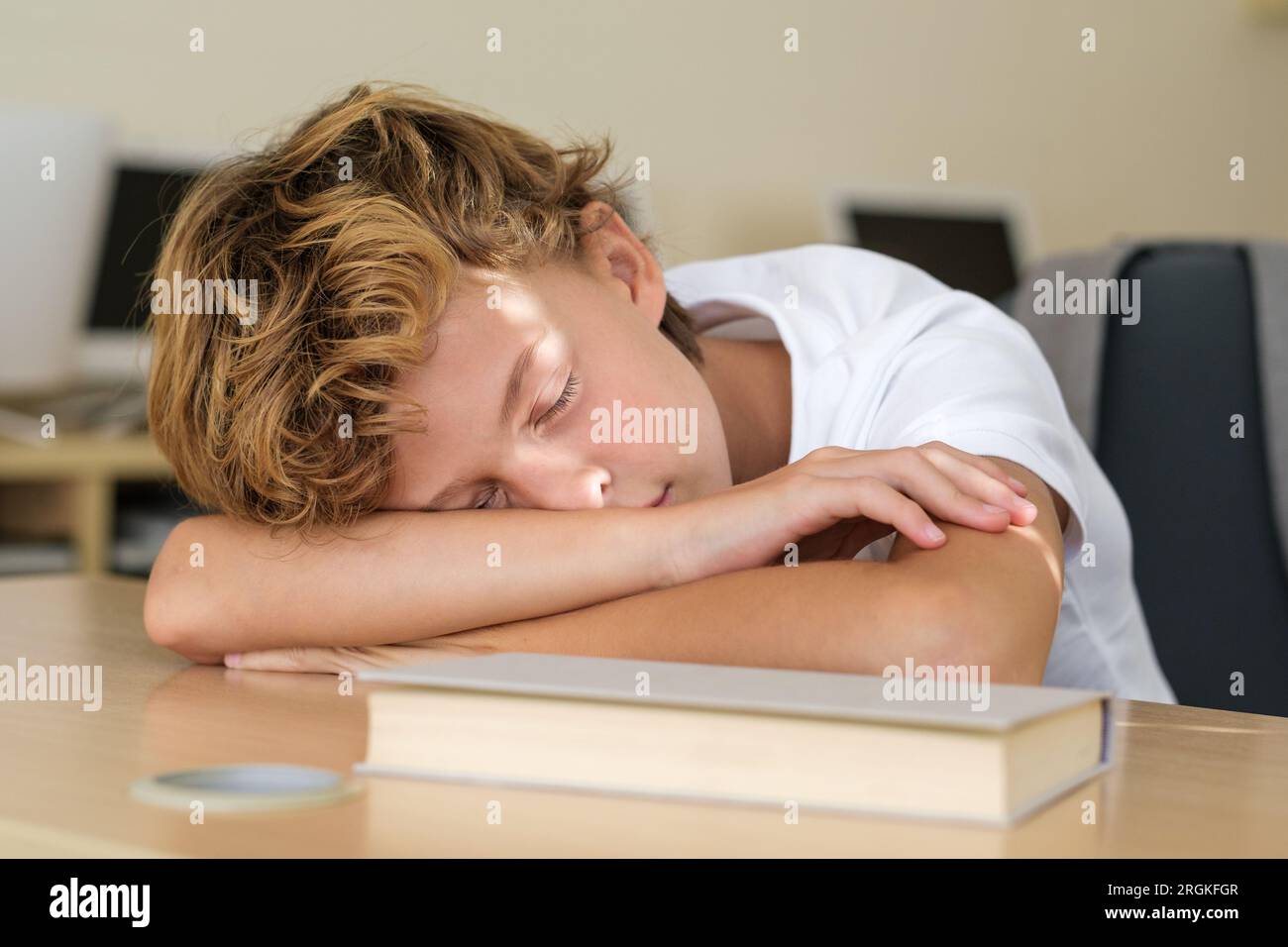 Scolaro stanco sdraiato su un tavolo di legno con libro e dormire durante la lezione in aula a scuola Foto Stock