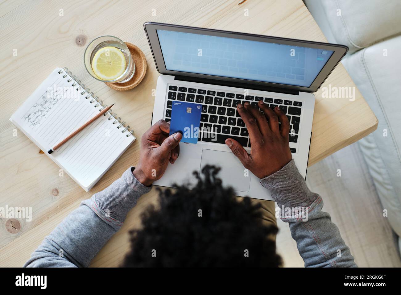 Dall'alto del raccolto irriconoscibile acquirente etnico maschio con carta di plastica che scrive sul netbook mentre facendo l'acquisto a casa Foto Stock