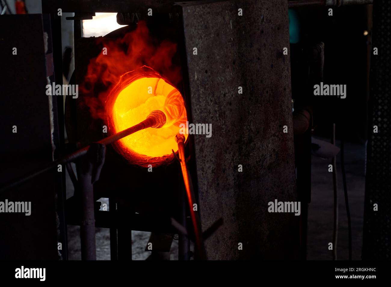 Tubo di soffiaggio con vetro liquido sotto forma di vaso di narghilè sulla punta posto nel forno con fiamme brucianti in fabbrica Foto Stock
