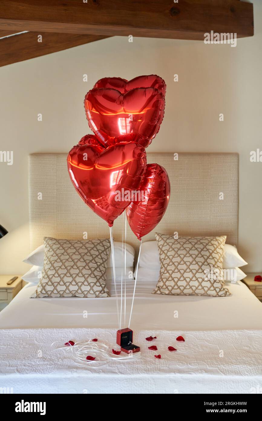 Camera da letto dell'hotel decorata con palloncini rossi a forma di cuore e  petali sparsi