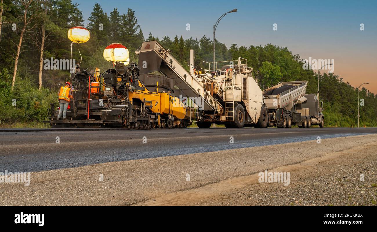 Pavimentazione di macchinari al tramonto su una strada governativa, di fronte a uno sfondo di alberi e lampioni, punto di estinzione Foto Stock