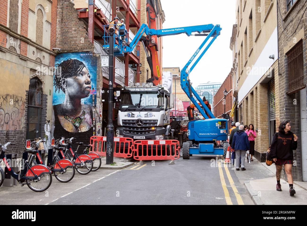 Strada chiusa bloccata da un camion da costruzione con gru e veicoli raccoglitori di ciliegie murale donna nera Spitalfields East London E1 England KATHY DEWITT Foto Stock