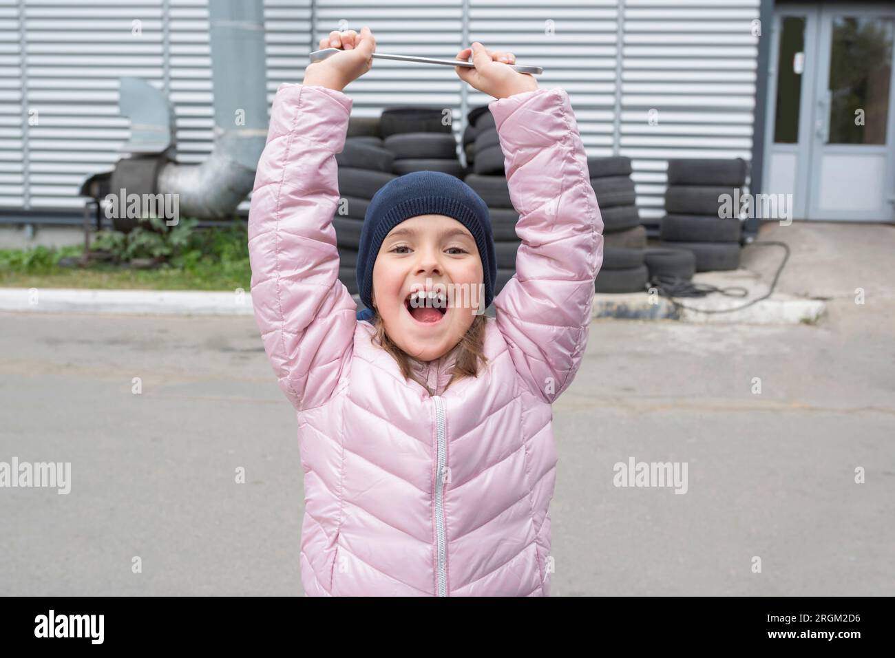 Ritratto di una bambina felice con una chiave inglese sullo sfondo del garage. Foto Stock