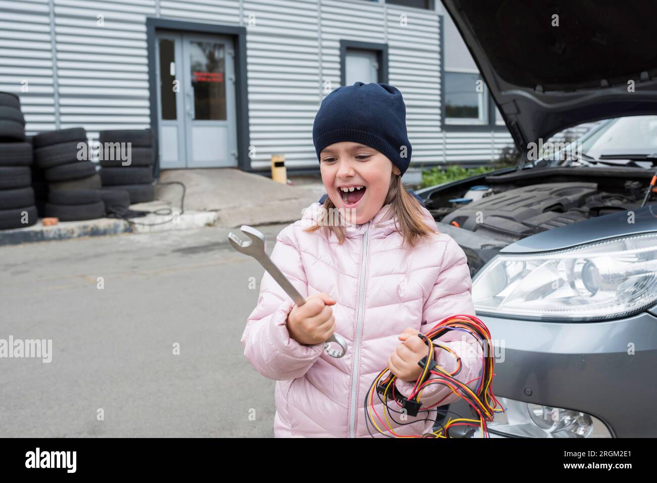 Ritratto di una bambina con una chiave inglese, sullo sfondo di un'auto. Concetto di riparazione automatica Foto Stock