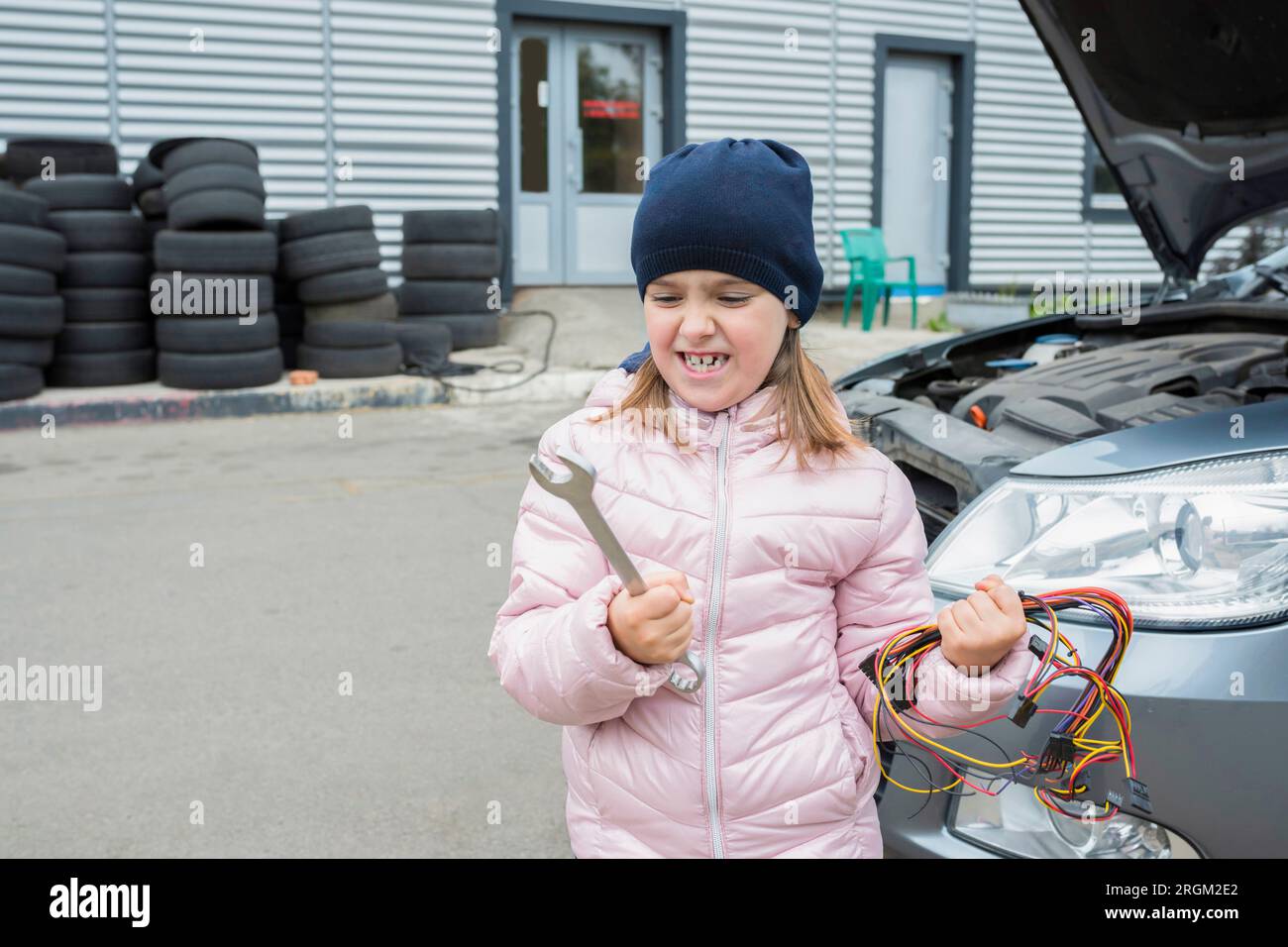 Ragazza emotiva con una chiave inglese e un mucchio di filo metallico, al servizio auto. Concetto di riparazione automatica Foto Stock