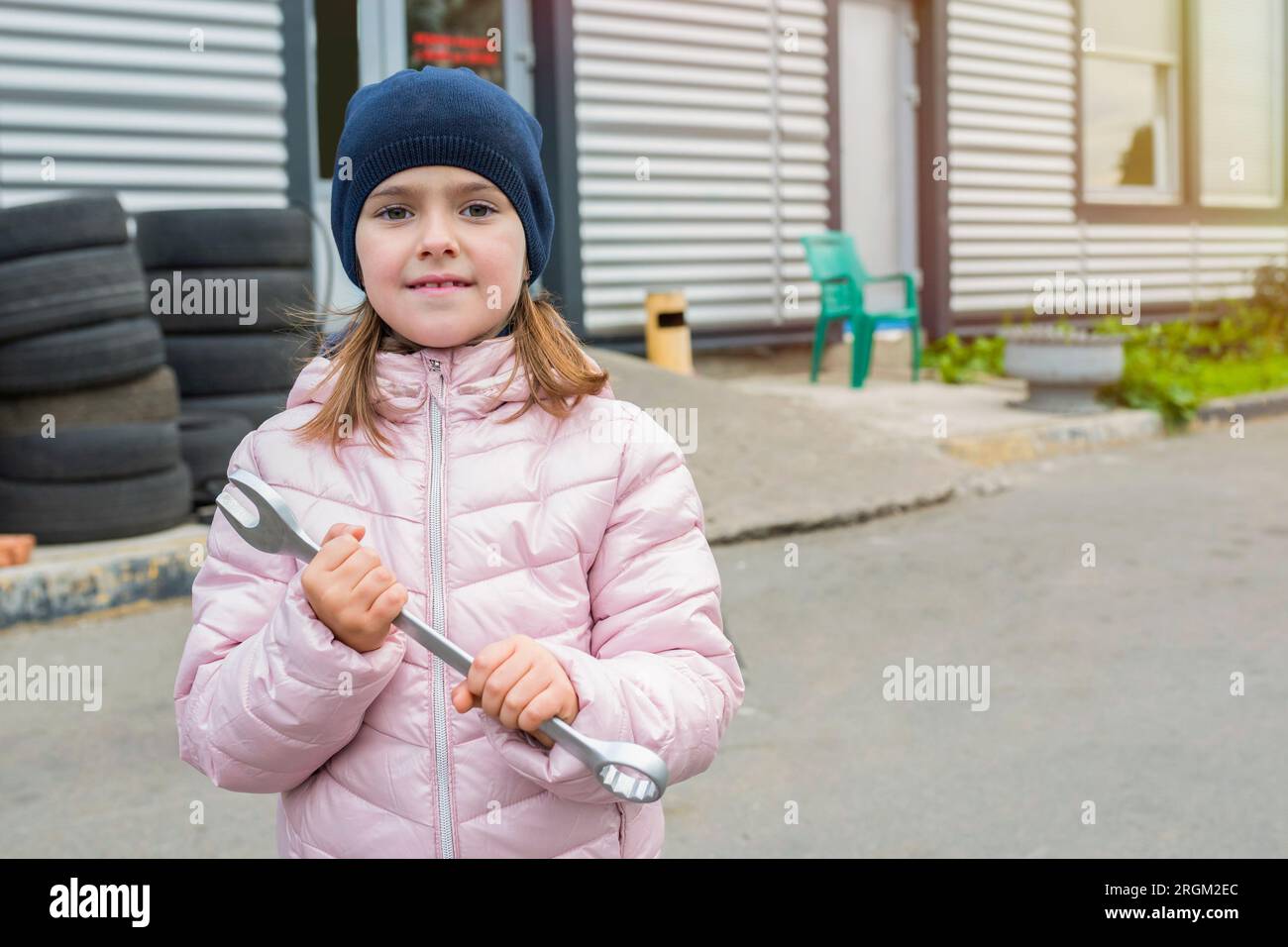 Bambina con una chiave inglese sullo sfondo del garage in una giornata di sole Foto Stock