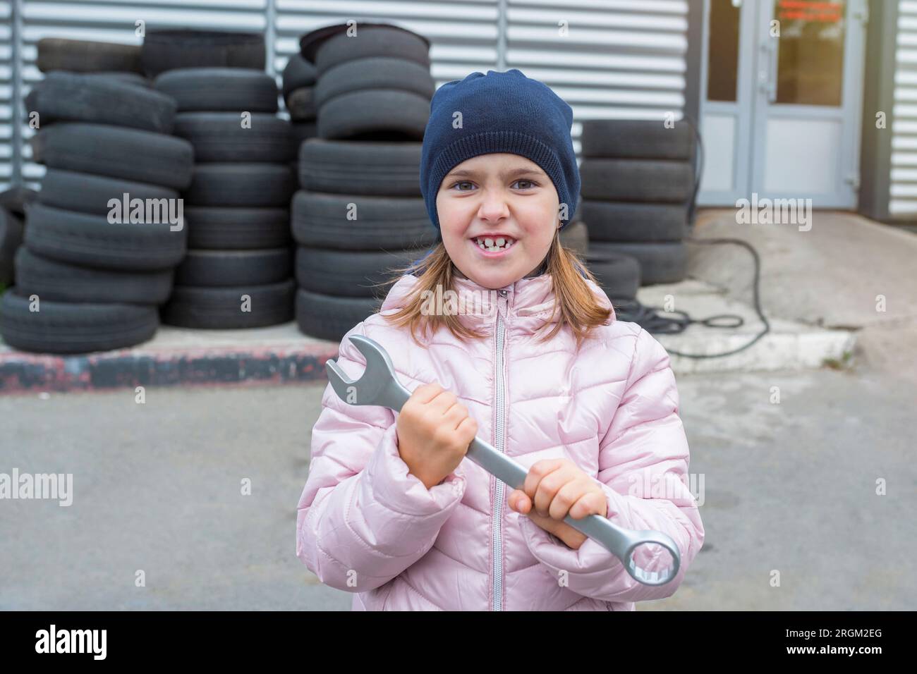 Ritratto di un bambino che tiene in mano una chiave inglese, sullo sfondo di un garage. Servizio di riparazione Foto Stock