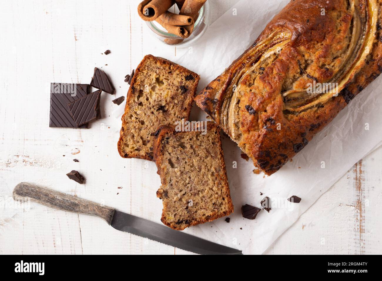 Pane alla banana umido a fette con avena e pezzi di cioccolato fondente su un tavolo di legno bianco Foto Stock