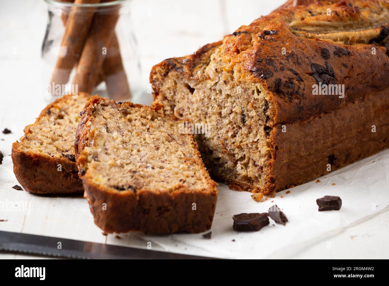 Pane alla banana umido a fette con avena e pezzi di cioccolato fondente su un tavolo di legno bianco Foto Stock