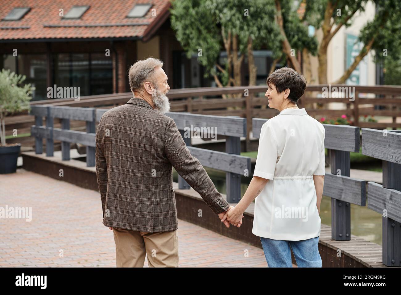donna felice e uomo barbuto che si tiene per mano, guardarsi l'un l'altro, appuntamento, romanticismo, coppia anziana Foto Stock