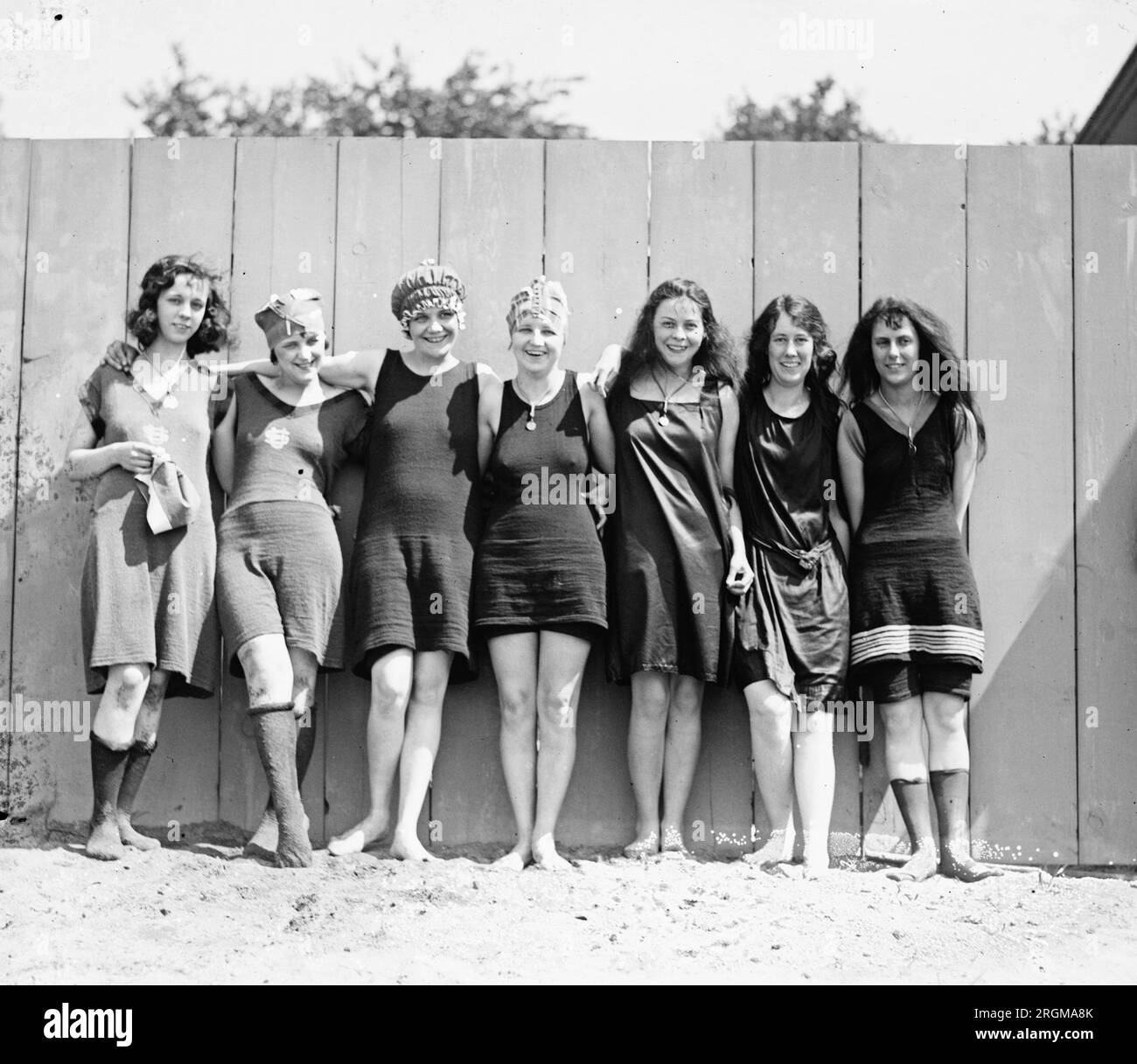 Giovani donne che indossano costumi da bagno, in piedi lungo una recinzione ca. 1920 Foto Stock