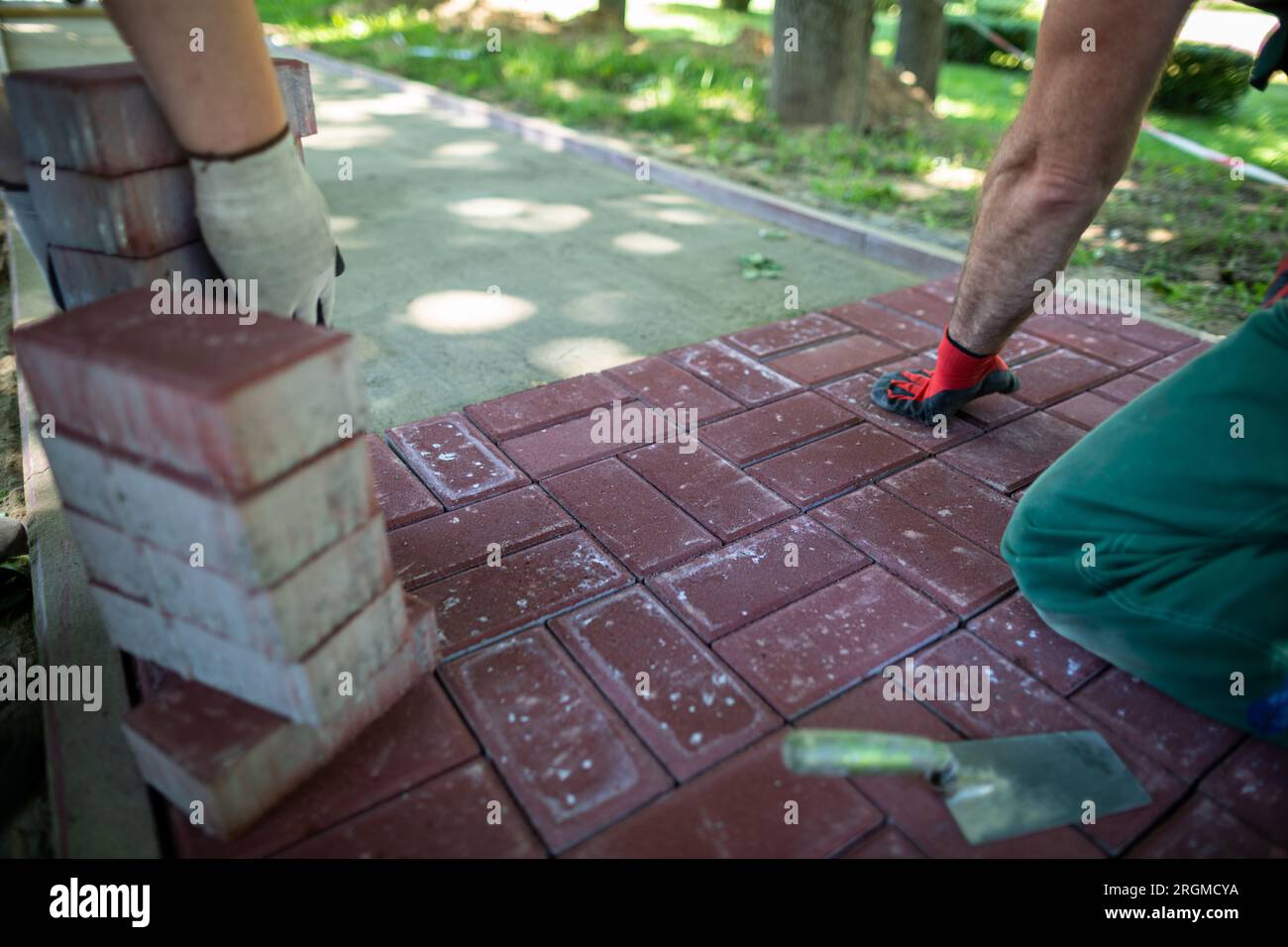 Un esperto lavoratore di pavimentazione si inginocchia durante la posa di pietre di pavimentazione. Foto Stock