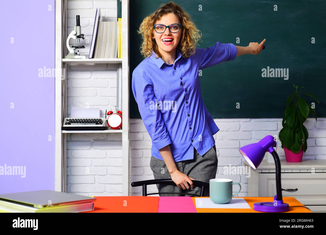 Insegnante sorridente in classe che punta il dito sulla lavagna. Studentessa all'università o al liceo. Istruzione, scuola e.. Foto Stock