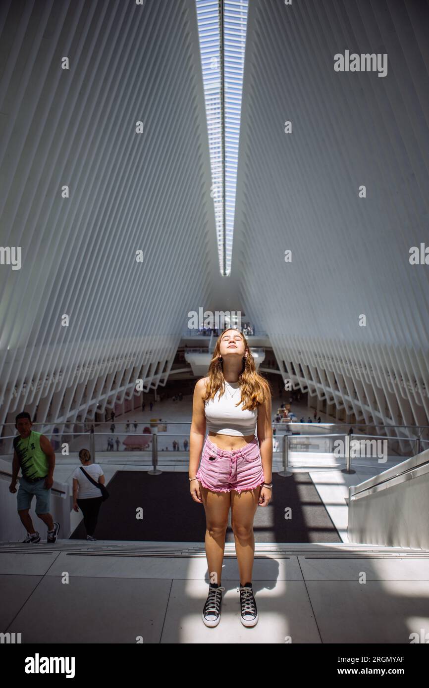 Adolescente che posa lo sguardo verso l'alto con una luce che la illumina nella stazione Oculus World Trade Center a Lower Manhattan, New York, USA Foto Stock