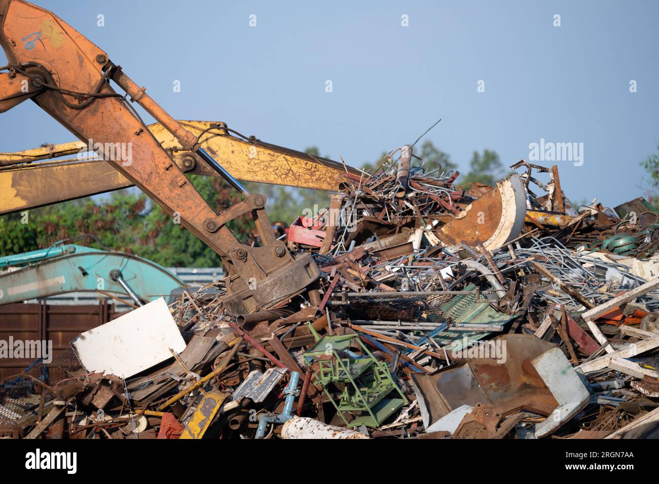 Il magnete dell'escavatore solleva i rottami d'acciaio dal cumulo di materiali riciclati presso il deposito di rottami in un impianto di riciclaggio. Escavatore con aspiratore elettromagnetico Foto Stock
