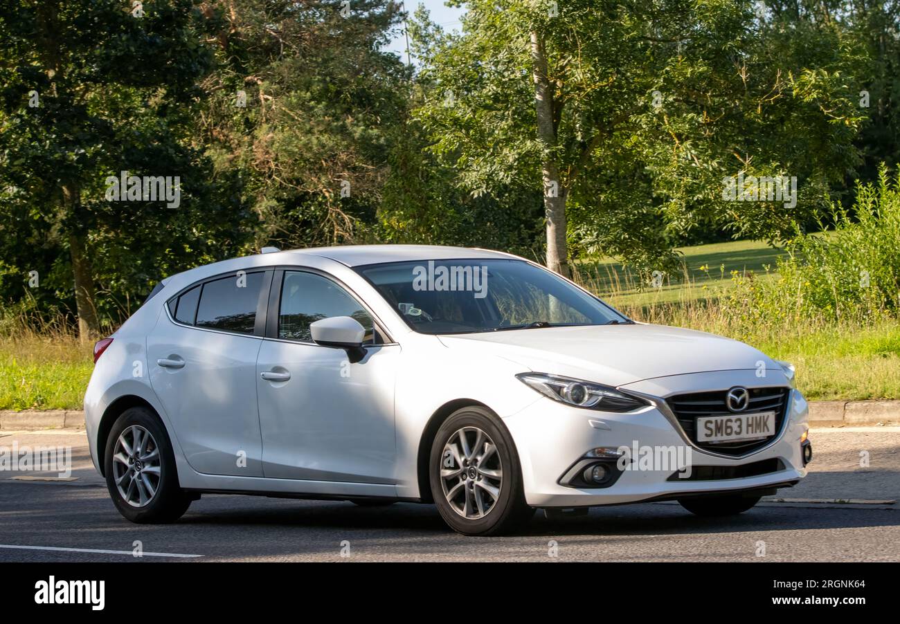 Milton Keynes, Regno Unito - 10 agosto 2023: 2014 auto Mazda 3 bianca che guida su una strada di campagna inglese. Foto Stock