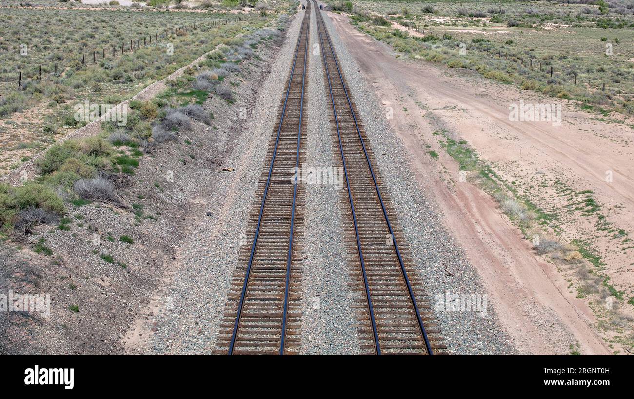 Percorso ferroviario in campagna che attraversa il deserto con bassa vegetazione, USA Arizona. Ferrovia in acciaio vuota con ghiaia e recinzione di lato. Sopra vi Foto Stock