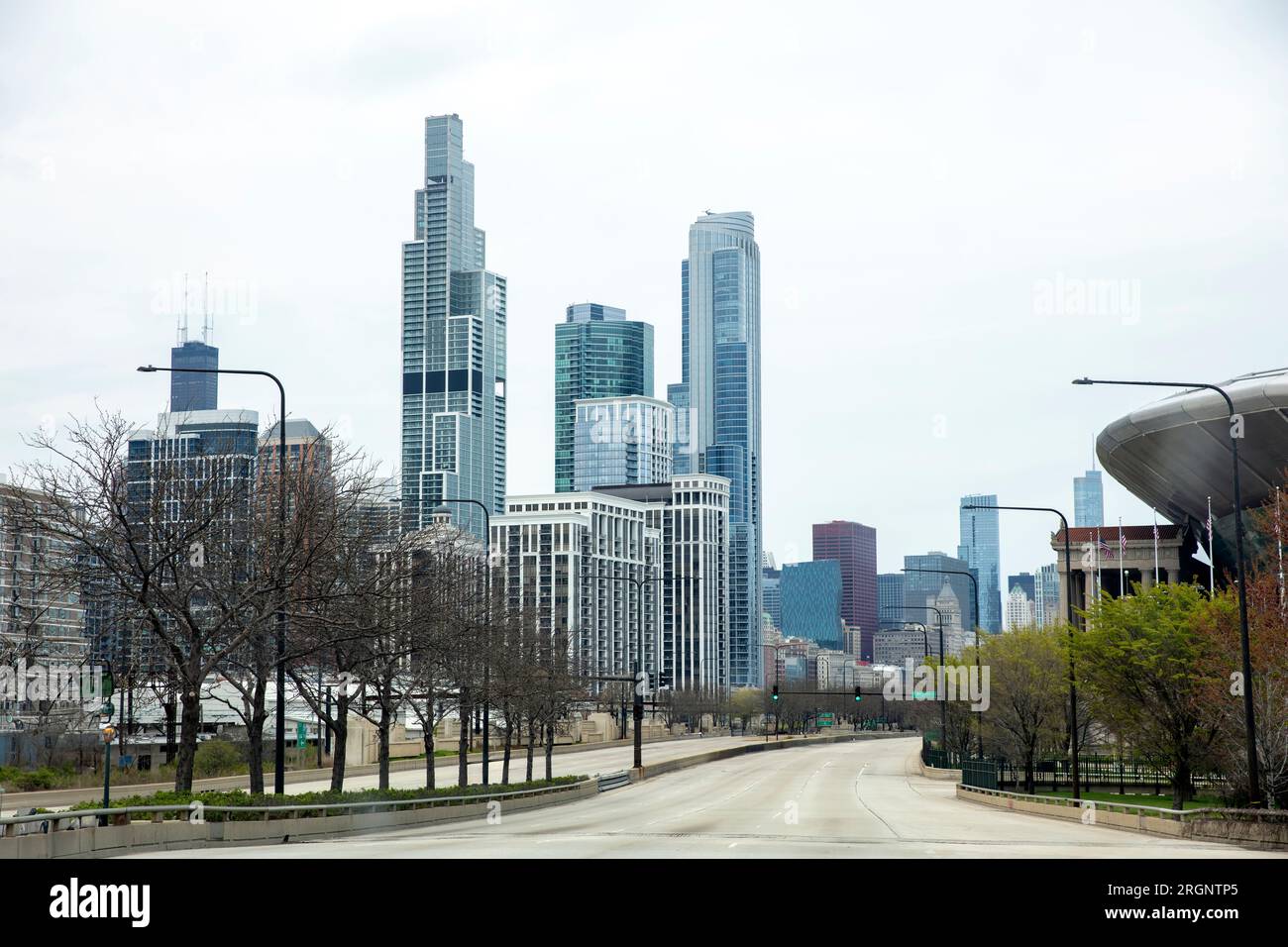 Chicago, Illinois, USA. Guida su una strada urbana vuota che conduce al centro città, all'edificio dei grattacieli, al semaforo, agli alberi, allo sfondo del cielo nuvoloso. Foto Stock
