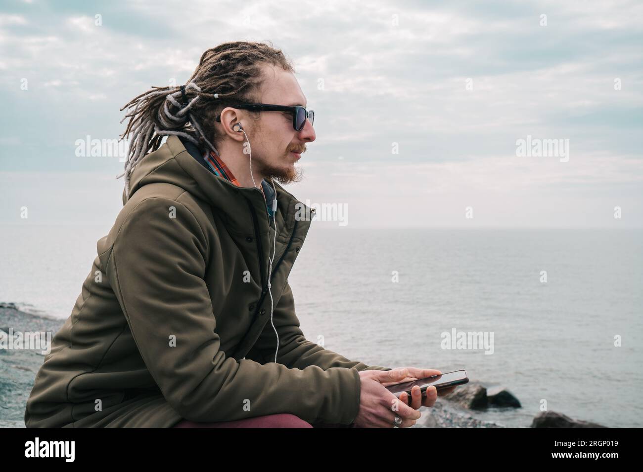 L'uomo solitario siede sulla riva del mare in un clima nuvoloso e cupo. Tristezza, depressione, e problemi mentali concetto, copia spazio Foto Stock