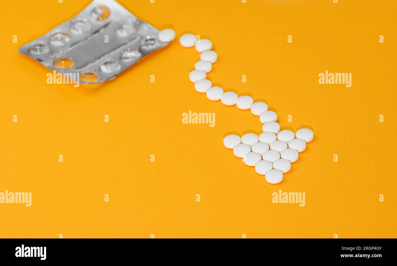 Concetto medico. Confezione blister a forma di freccia su sfondo arancione. Foto Stock