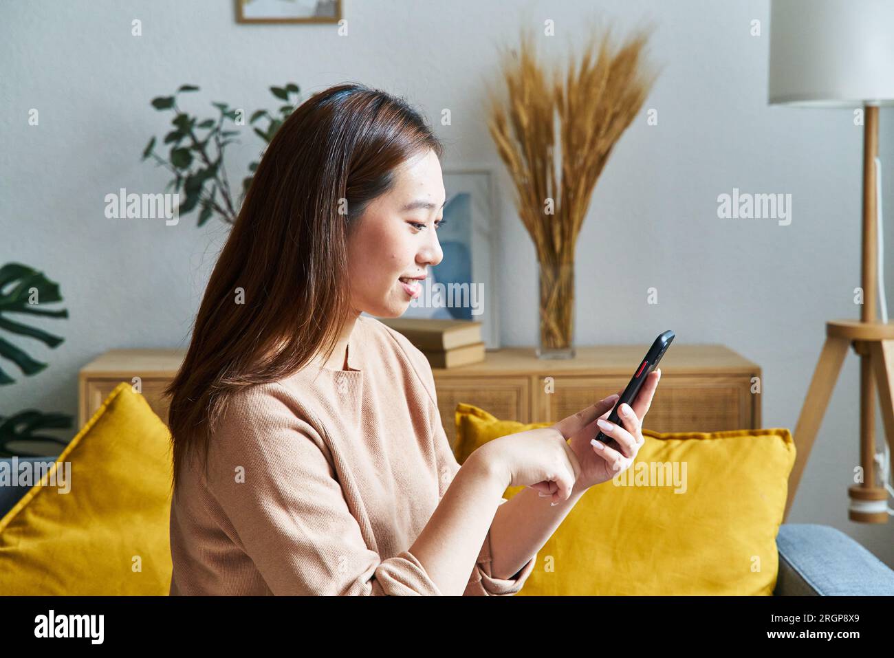 Donna seria che usa il cellulare seduto su un divano Foto Stock