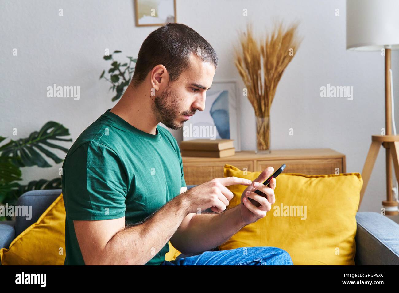 Un uomo serio che usa il cellulare seduto su un divano Foto Stock
