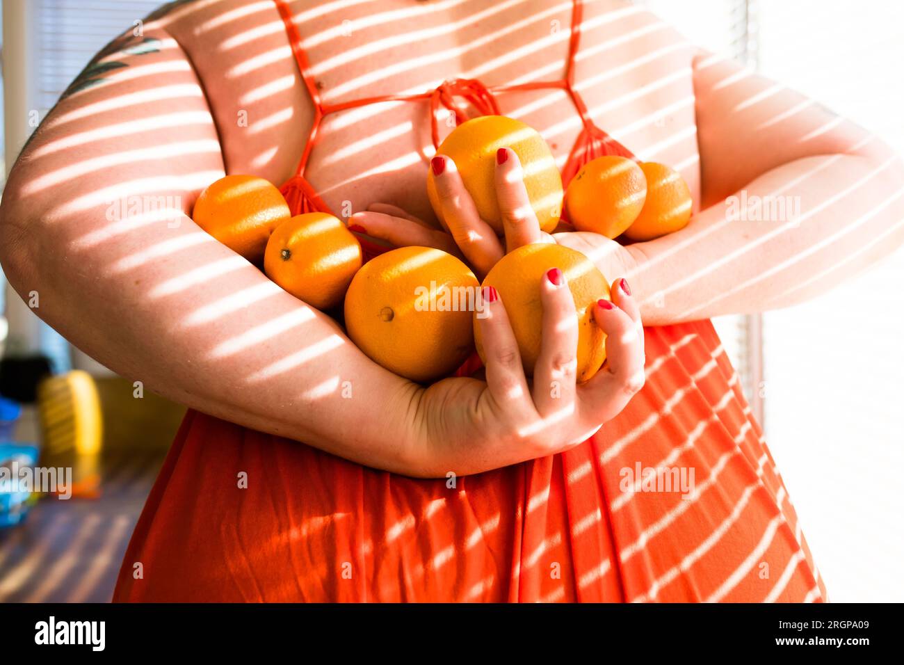 tenendo sette arance dietro la schiena con un vestito arancione Foto Stock
