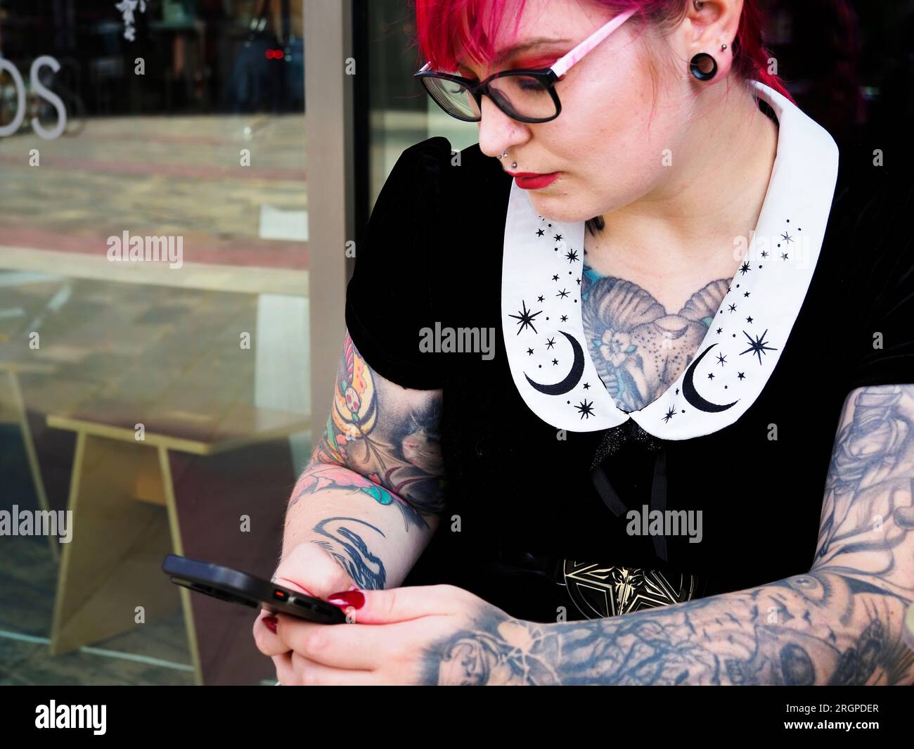Donna di vent'anni con capelli rossi tinti e tatuaggi che indossa occhiali con uno smartphone a Leeds West Yorkshire in Inghilterra Foto Stock