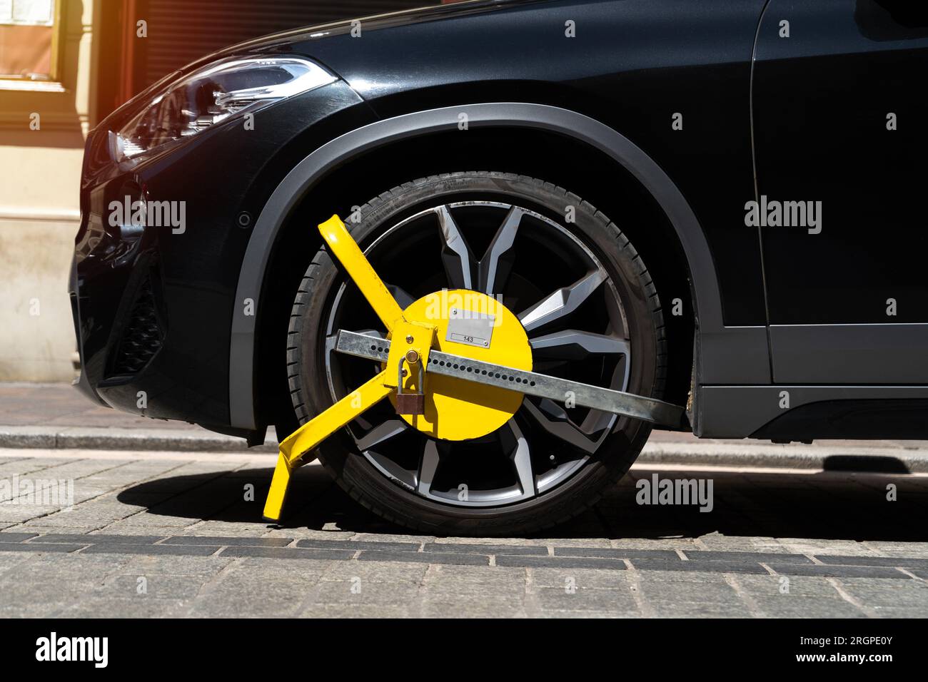 Ruota del veicolo bloccata da un blocco metallico giallo o da un morsetto. Violazione illegale del parcheggio del veicolo in una zona soggetta a restrizioni. Foto Stock