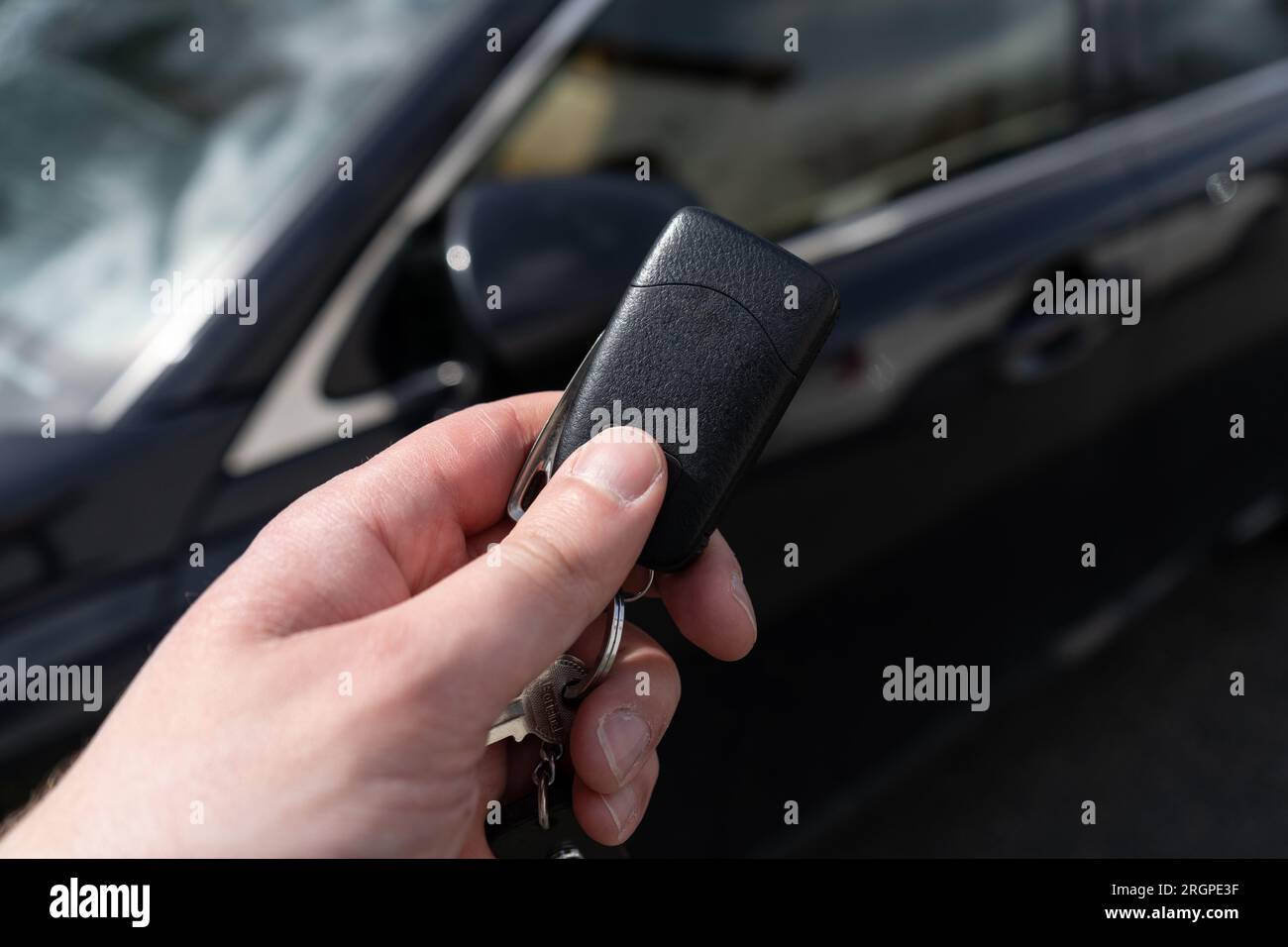 Mano dell'uomo che tiene la chiave dell'auto remota, accanto a un veicolo nero. Foto Stock