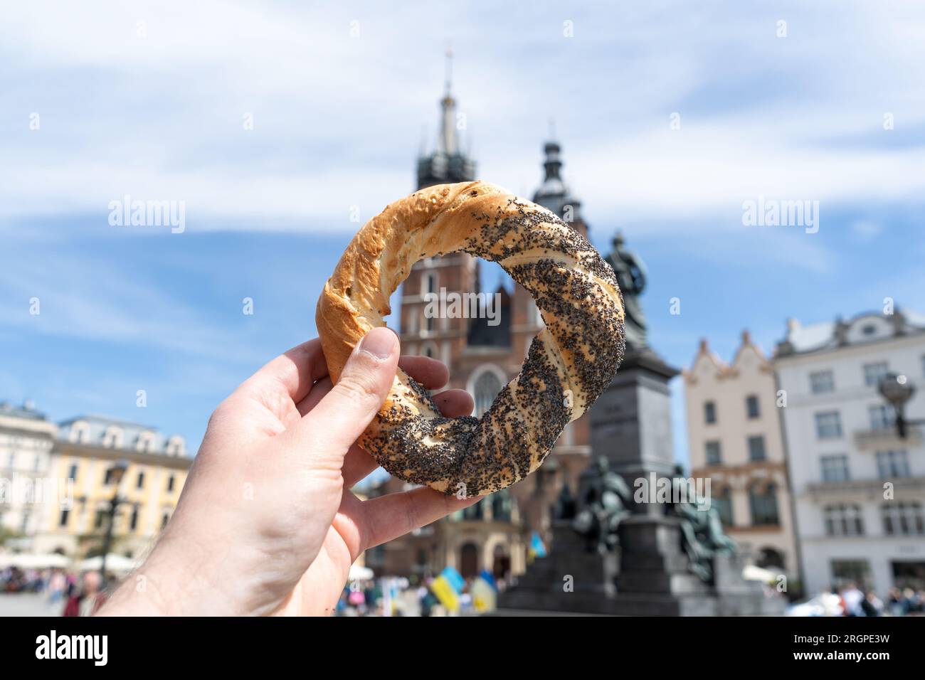 Mano che regge il pretzel obwarzanek krakowski sulla piazza principale del mercato di Cracovia, vicino a St Chiesa della Basilica di Maria. Cibo Krakowskie obwarzanki a Cracovia, Polonia. Foto Stock
