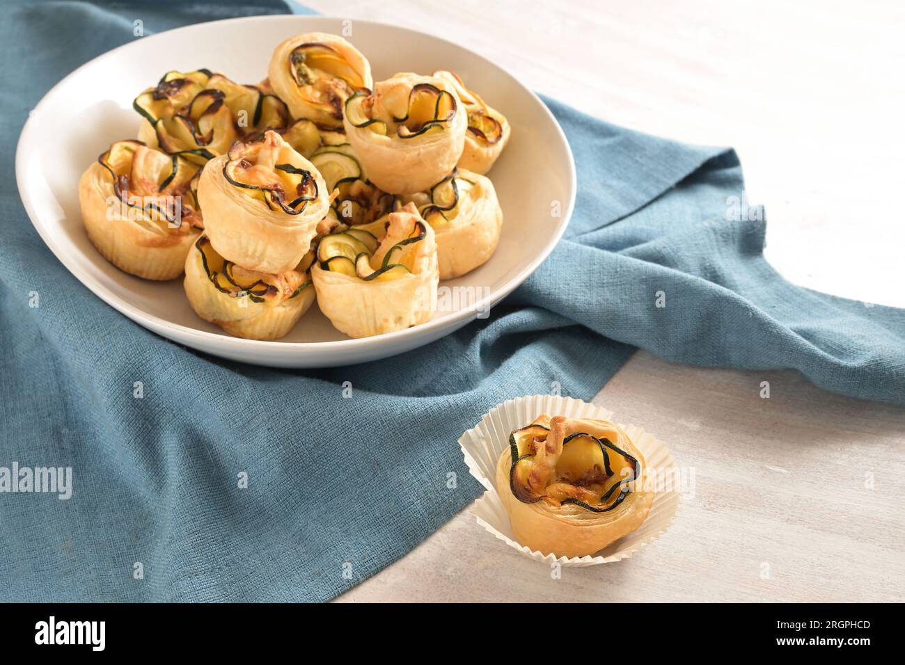 Muffin di pasta sfoglia arrotolati con fette di zucchine, snack vegetariani con finger food in una ciotola bianca su un tovagliolo blu per un buffet caldo o freddo, copia Foto Stock