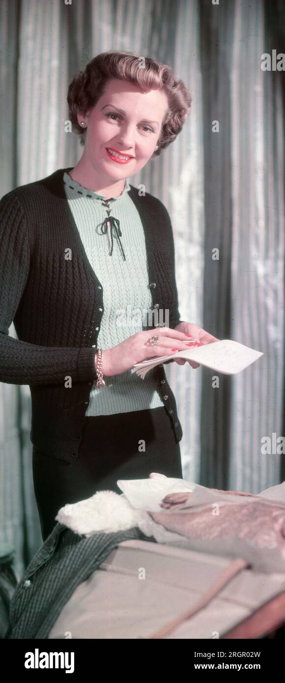 Anni '1950, immagine storica che mostra la moda inglese in questa camera del era....inside a, una donna elegante e attraente che indossa un cardigan di lana chiaro sopra una delicata camicetta, abiti che riflettono le sue caratteristiche femminili e delicate e lo stile raffinato e sofisticato, Inghilterra, Regno Unito. Gli anni '50 furono il decennio del cardigan. Foto Stock