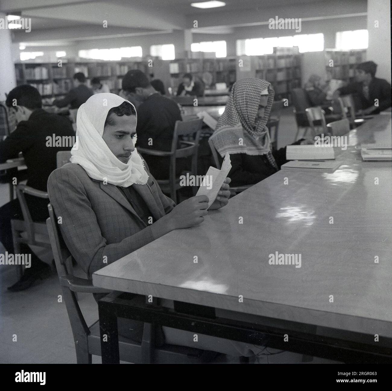 Anni '1960, storici, due uomini arabi, che indossano una tradizionale testata o Keffiyeh, seduti a un tavolo in una biblioteca a leggere, Arabia Saudita. Foto Stock