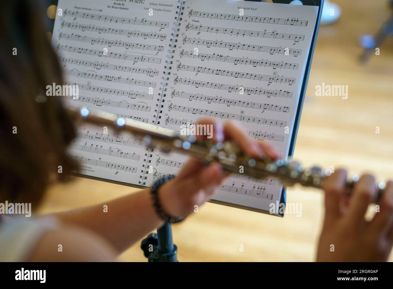 Vista posteriore di una donna che suona un flauto trasversale mentre legge uno spartito musicale Foto Stock
