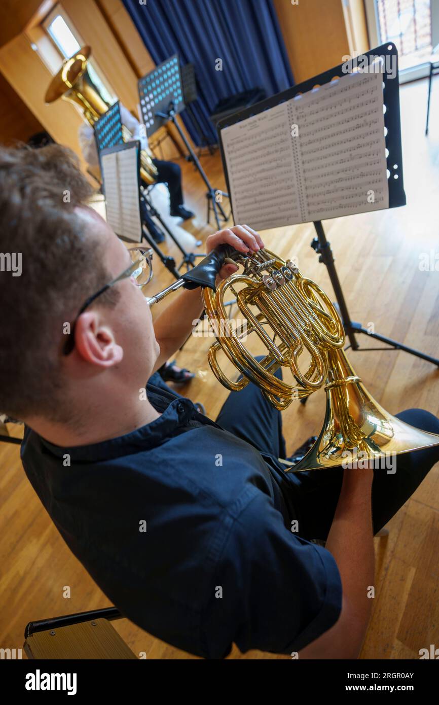 Musicista che suona il corno francese mentre guarda gli spartiti durante la pratica della band filarmonica Foto Stock