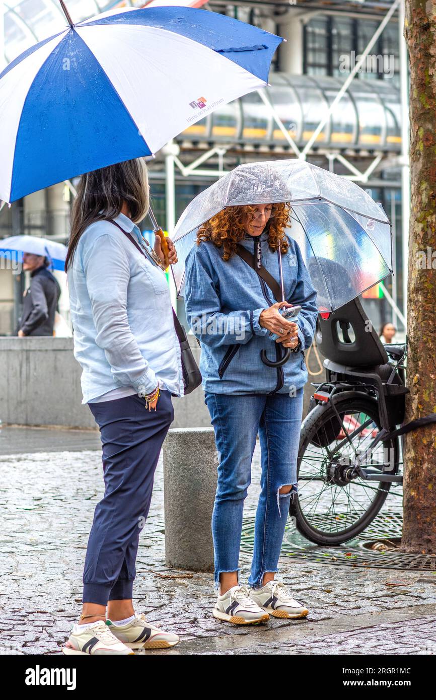 Due donne che si rifugiano sotto gli ombrelli nella piovosa Parigi, Francia. Foto Stock