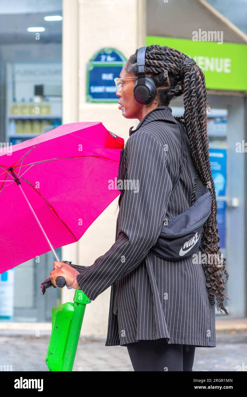 Giovane donna di colore con parrucchiere intrecciato e ombrello nella piovosa Parigi, Francia. Foto Stock