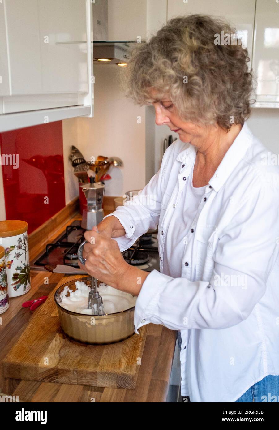 Cuoca casalinga sbattendo a mano gli albumi a punte rigide per preparare una mousse al cioccolato o una meringa Foto Stock