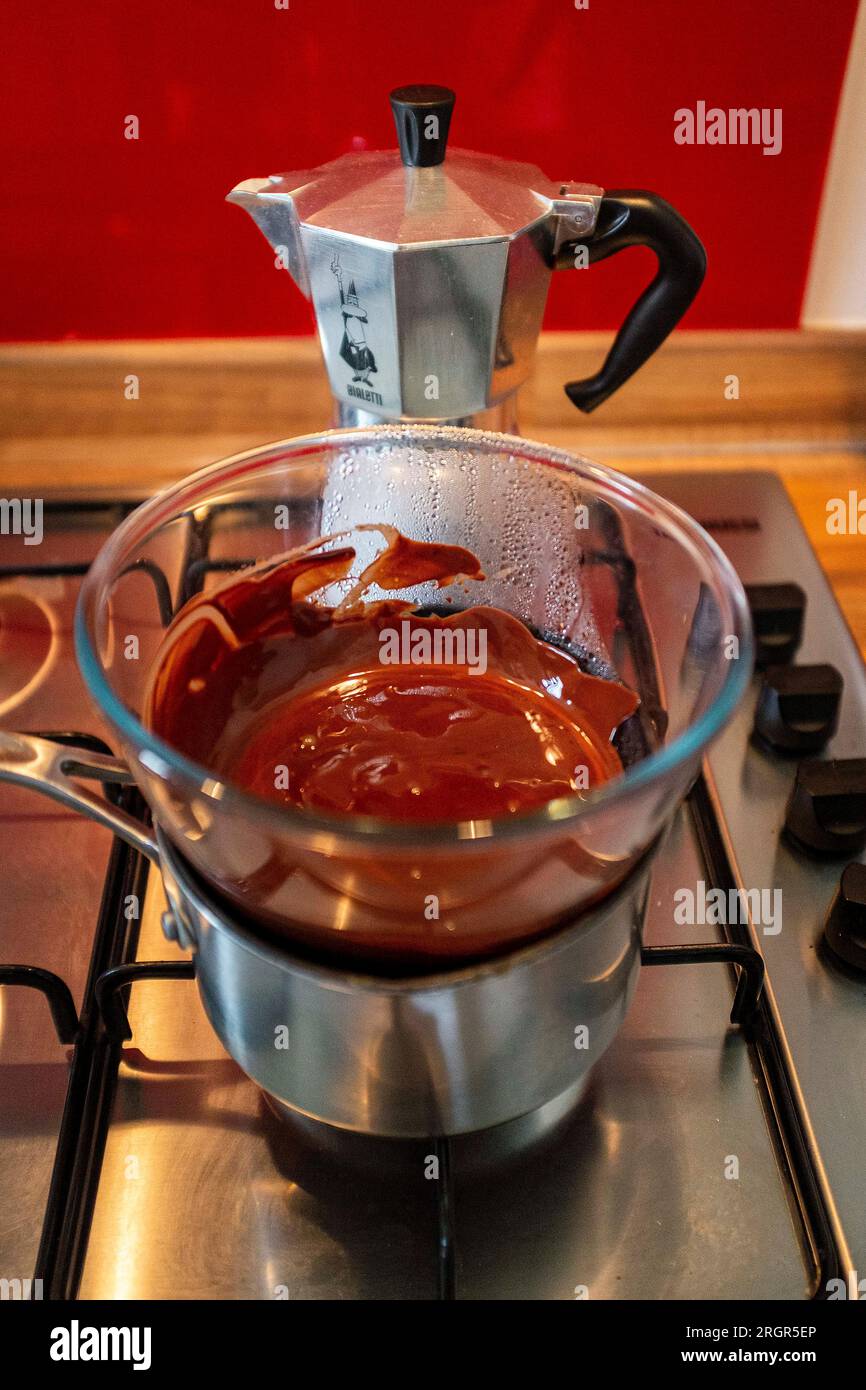 Sciogliere il cioccolato fondente in una ciotola di vetro su una pentola calda su un piano cottura a gas in cucina Foto Stock
