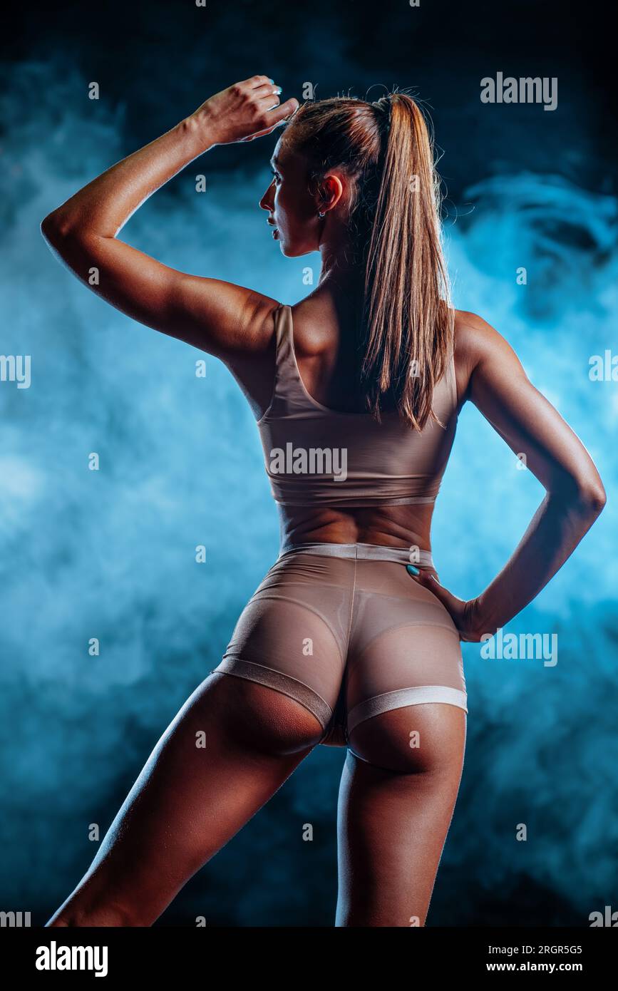 Vista posteriore di una giovane donna sportiva sexy e sottile su sfondo fumé scuro Foto Stock