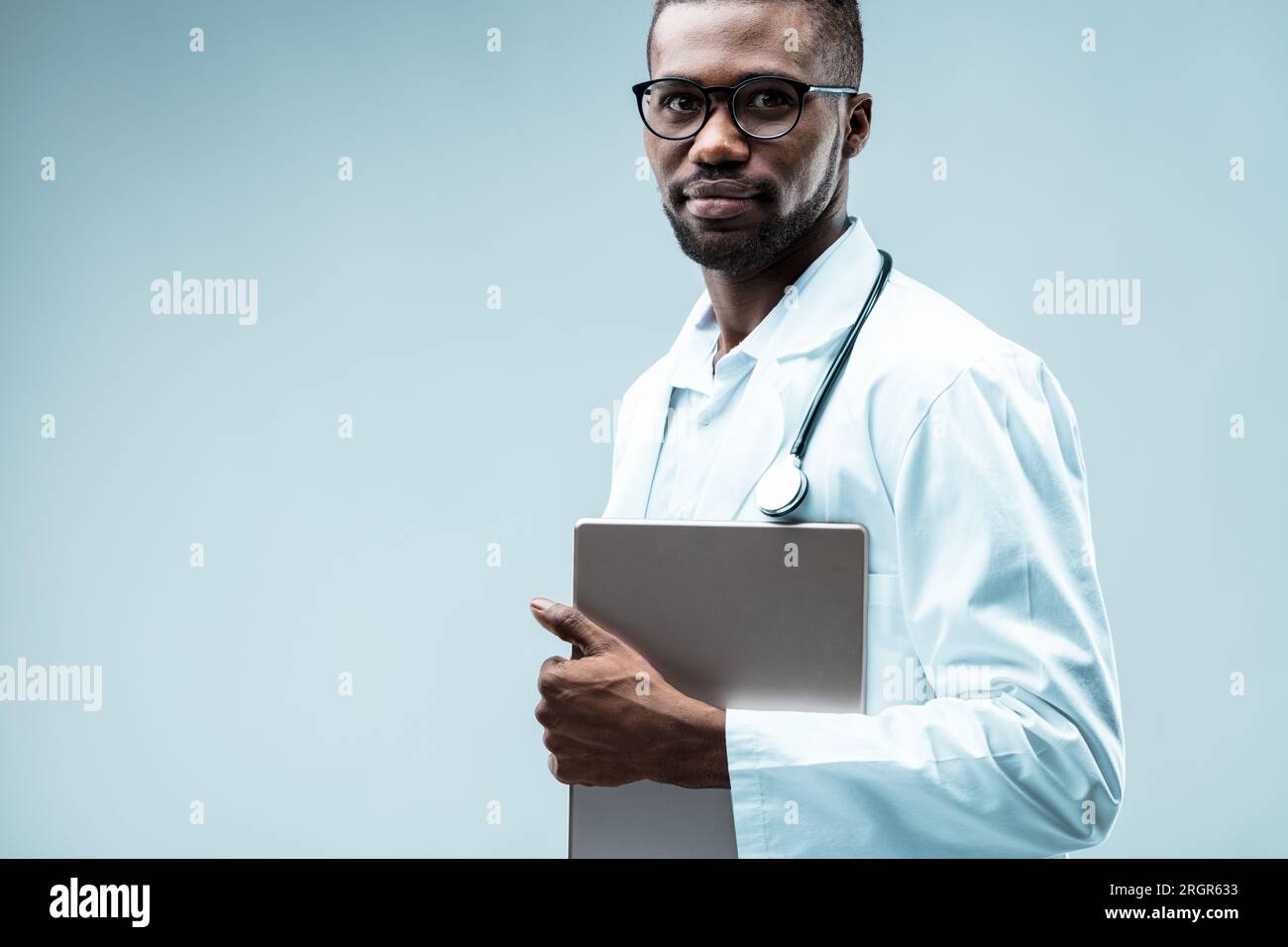 Medico nero con un tablet, trae vantaggio dalla tecnologia digitale. Indossa camice bianco, stetoscopio, vari gradi, tirocini ed è anche attraente Foto Stock