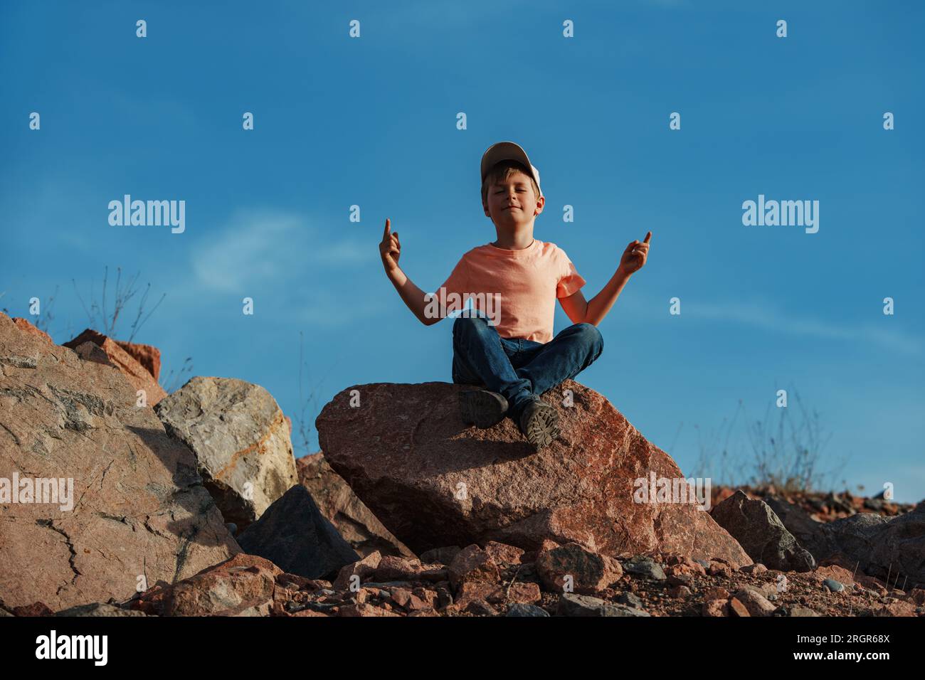 Un ragazzo seduto in meditazione poggia sulla roccia nelle montagne Foto Stock
