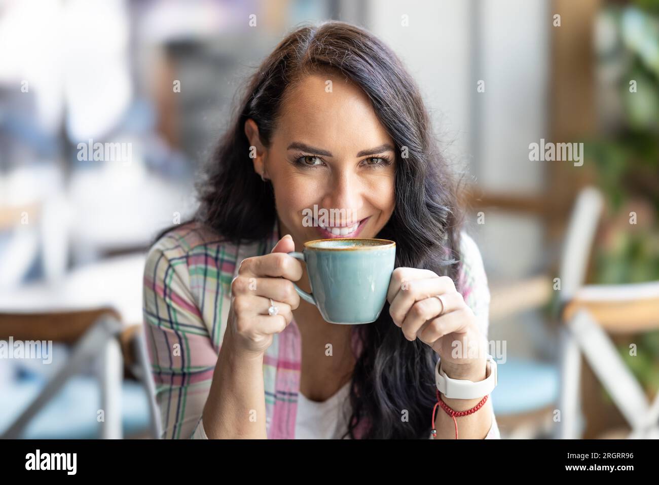 Una bruna attraente di buon umore gusta un cappuccino in una caffetteria. Foto Stock