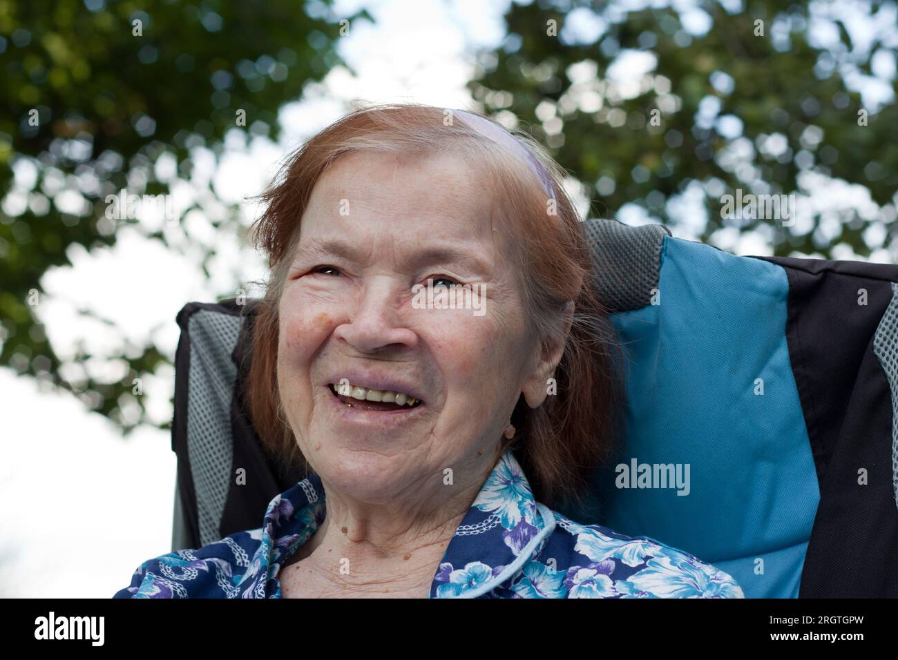 Ritratto della nonna anziana sorridente in giardino a casa. anziana con oltre 80 ridere, gioire, rilassarsi, sedersi in sedia, nella natura. Estate. Vecchio Foto Stock